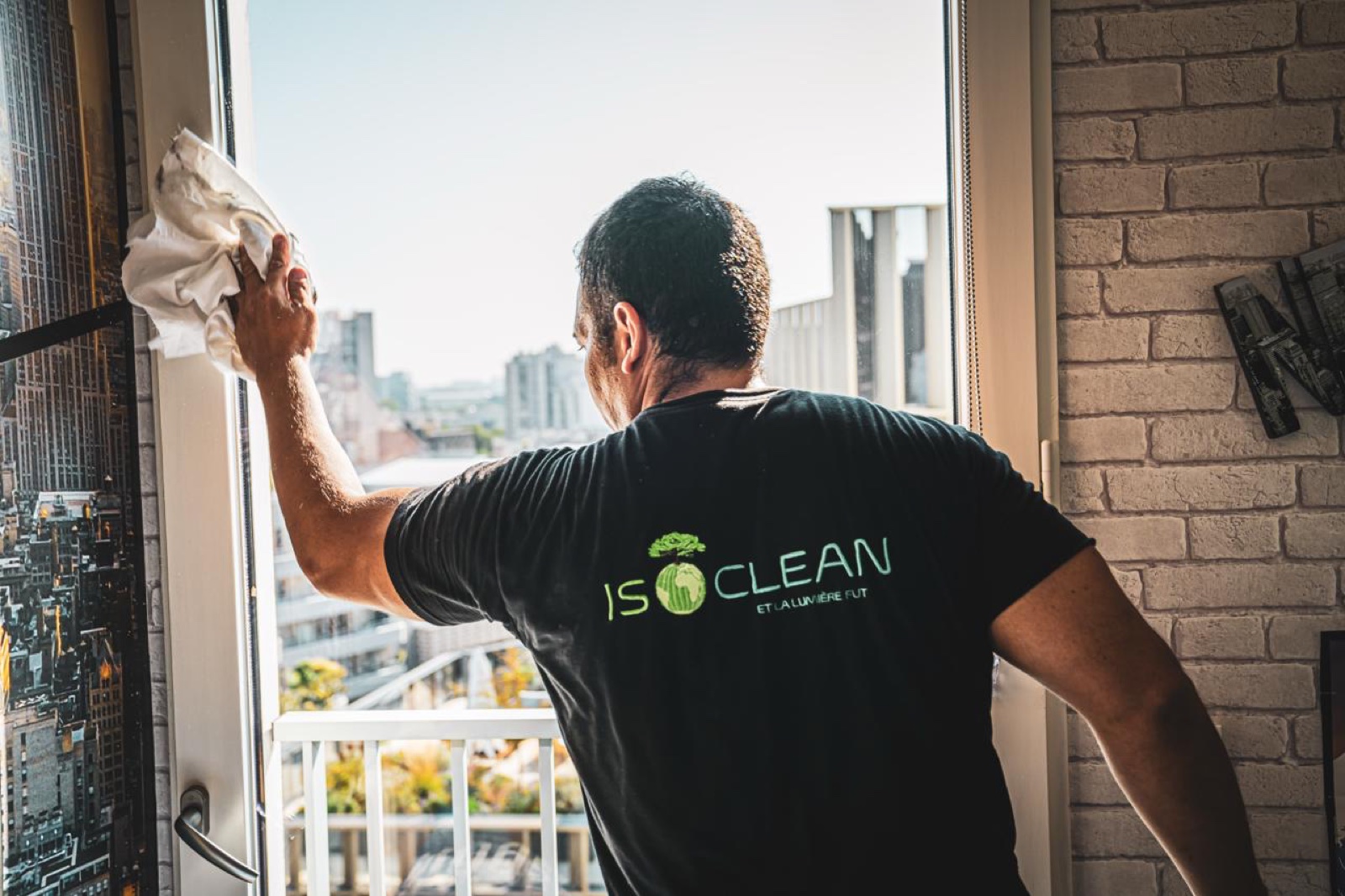 Agent ISOCLEAN en t-shirt de la marque nettoyant une vitre, vue sur la ville